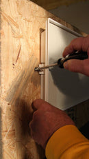 Person using a screwdriver to install a panel on wooden wall.